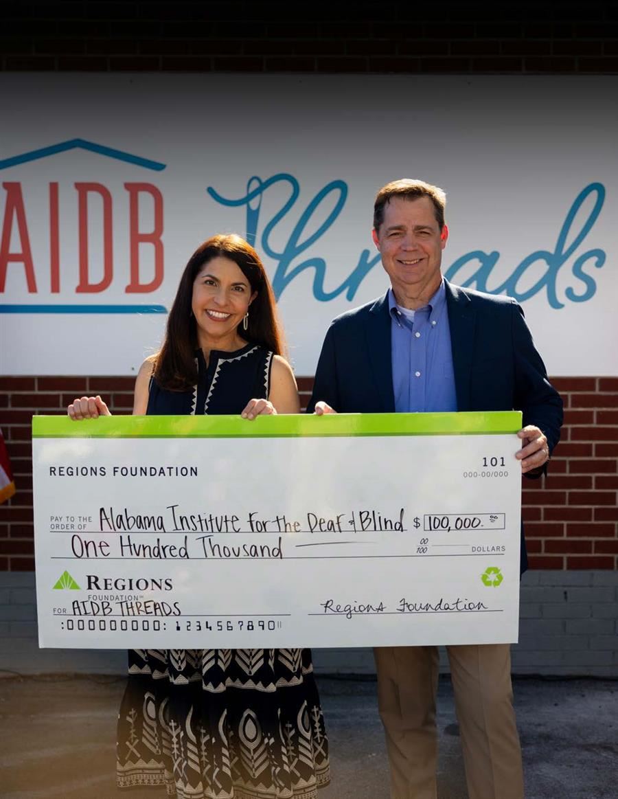  Two people holding an oversized $100,000 check from Regions Foundation to AIDB.